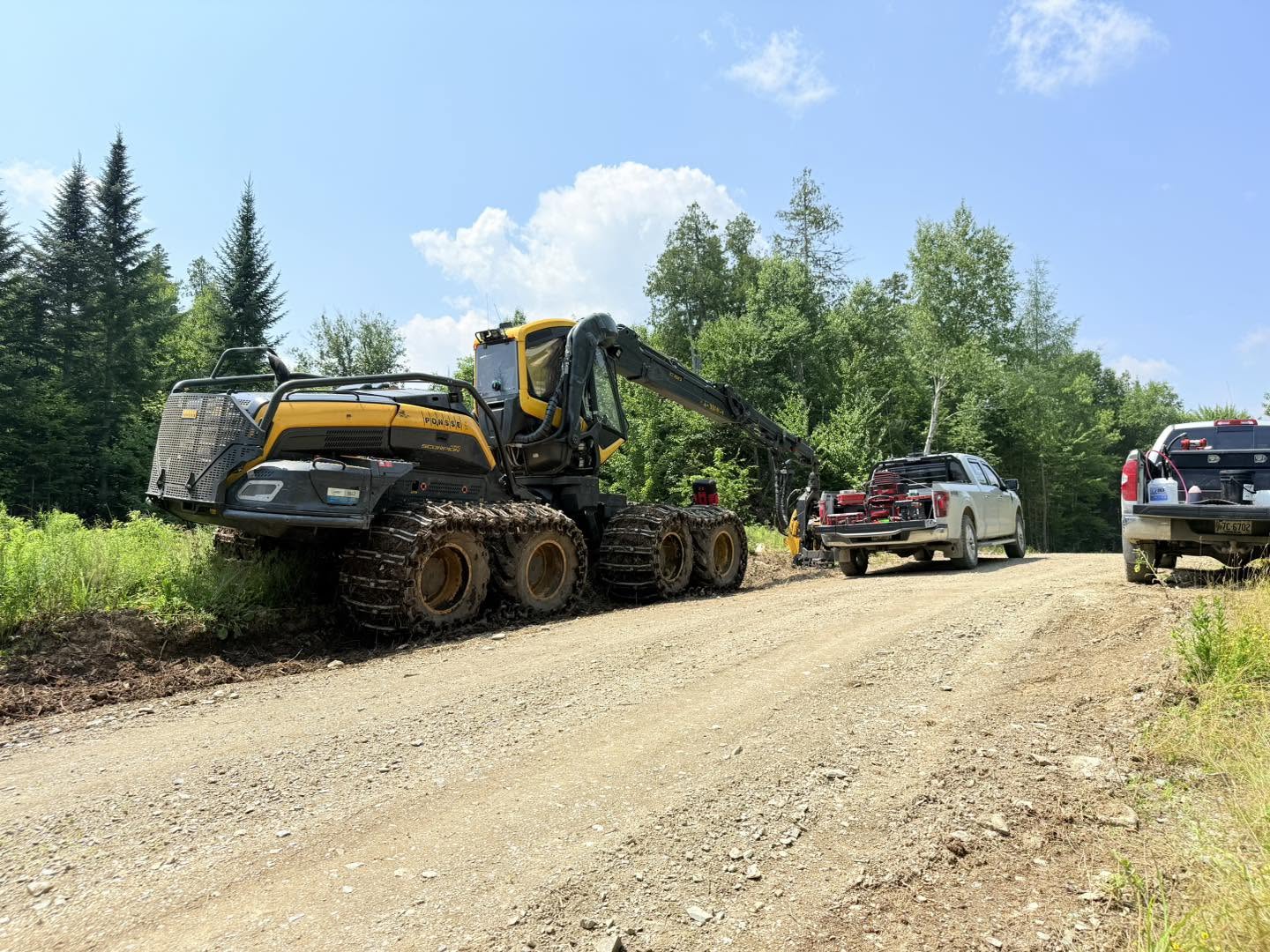 Radio-equipped work trucks and a forestry harvester parked on a Maine logging road