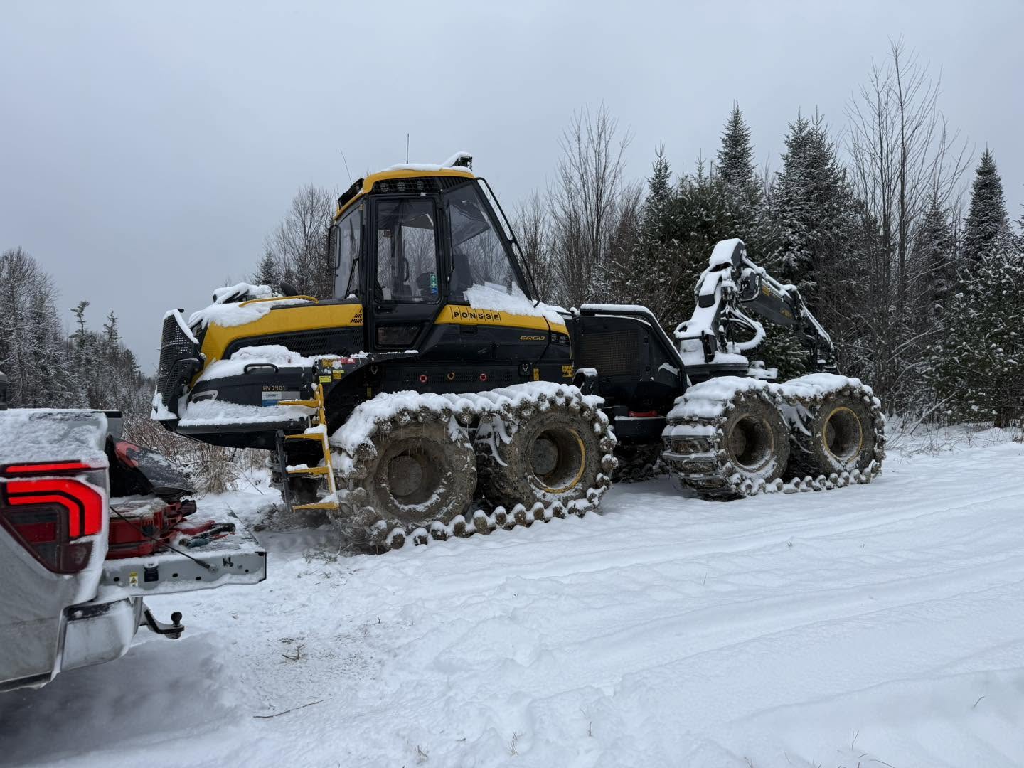 Forestry harvester equipped with radio antenna, parked in snow on a logging road